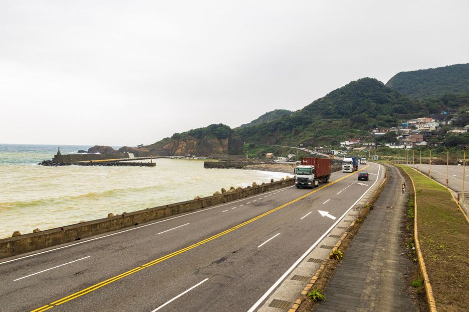 Trucks traveling on a coastal road with beautiful mountain and ocean views, enhancing logistics imagery.